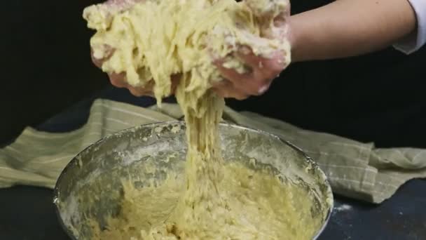 person in chef uniform by hands slowly kneads soft yeast dough in metal bowl - Záběry, video
