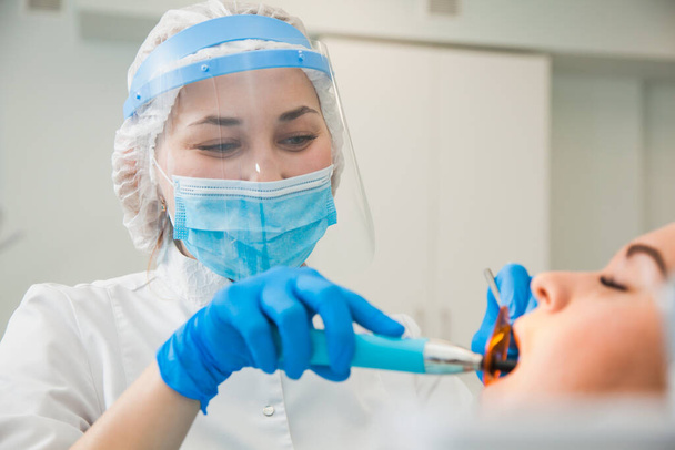 Dentystka leczy ubytek zębów w niebieskich rękawiczkach i masce ochronnej. - Zdjęcie, obraz