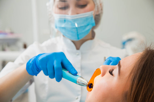 Женщина-дантист, вылечивающая зубы в синих перчатках и защитной маске
. - Фото, изображение