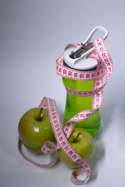 Červená měřicí páska přes zelenou sportovní láhev a zelené jablko. Dieta a zdravý život, hubnutí, sportovní koncept. Horní pohled. Rozumím. Izolovaný. Bílé pozadí - Fotografie, Obrázek