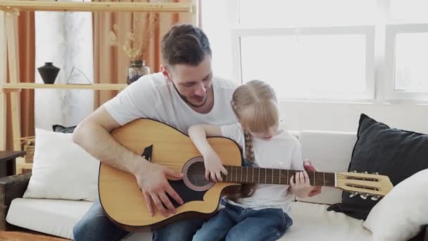 Padre joven enseña a su hija a tocar la guitarra en casa
 - Metraje, vídeo