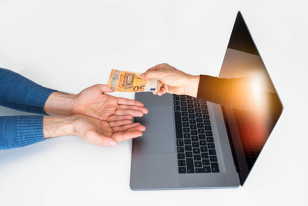 Online transaction. An arm comes out of a laptop to deliver money to a customer or taxpayer. It can represent an online transaction or money gain. - Photo, Image