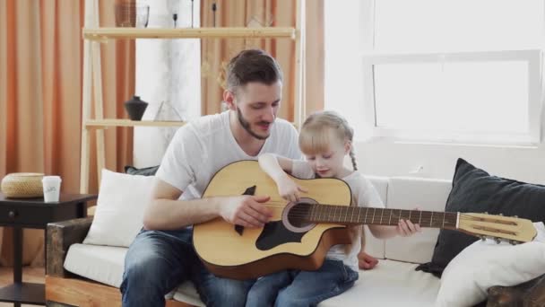 Padre joven enseña a su hija a tocar la guitarra en casa
 - Metraje, vídeo