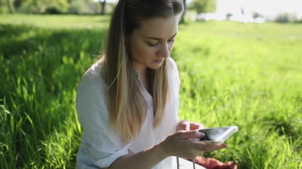 Blond mother talking on the phone outdoors. Young woman on grass - Video, Çekim