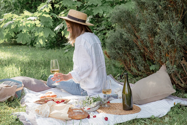 Piknikte hasır şapkalı bir kadın elinde bir bardak şarap tutuyor. Yaz dönemi maceraları - Fotoğraf, Görsel