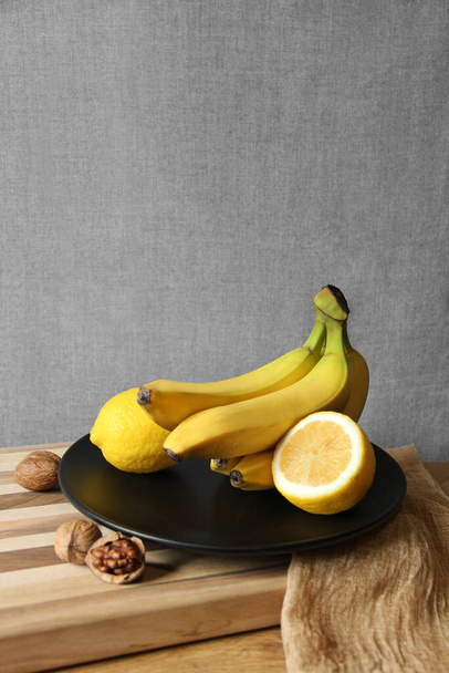 A bunch of bananas on a black plate. Yellow fruit. Contrast of colors. Bananas and lemons. Tropical fruits. Ripe bananas - Foto, afbeelding