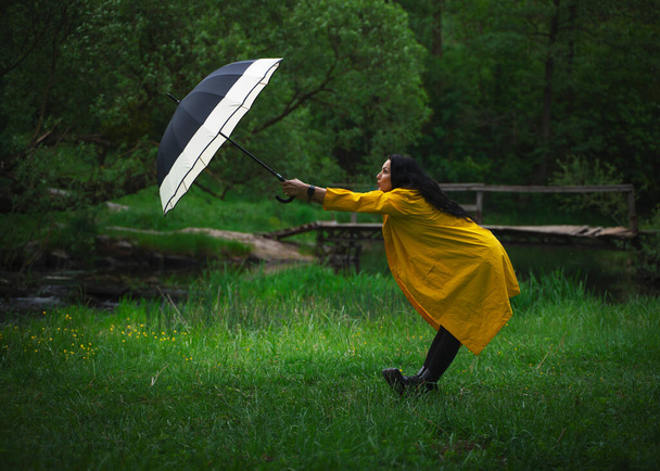 beautiful young girl in a yellow raincoat, with an umbrella in the garden, rainy spring, beautiful and stylish clothes, fashion - Photo, Image