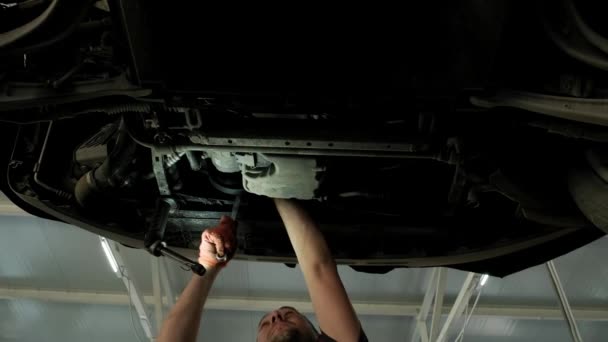Otomobil tamircisi garajda araba kaldırma makinesinin altında çalışıyor. Otomobil tamirhanesi, araba servisi, tamirat..    - Video, Çekim