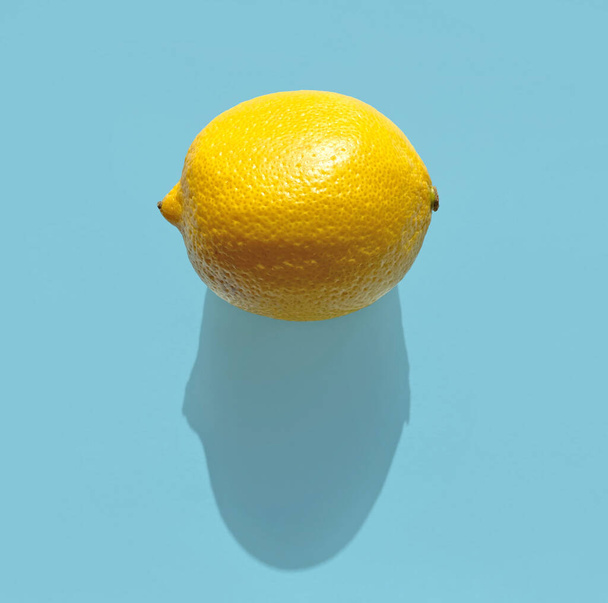 frische Zitrone mit langem Schatten auf blauem Hintergrund, Draufsicht - Foto, Bild