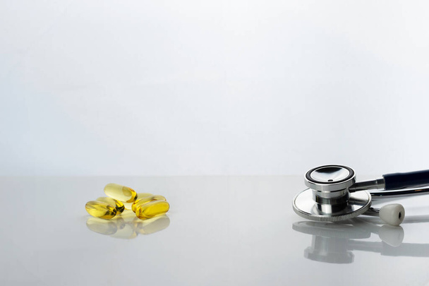 die gelbe Fischöl-Pille Nahrungsergänzung mit Metall-Stethoskop für ärztliche Diagnose auf weißem Hintergrund   - Foto, Bild