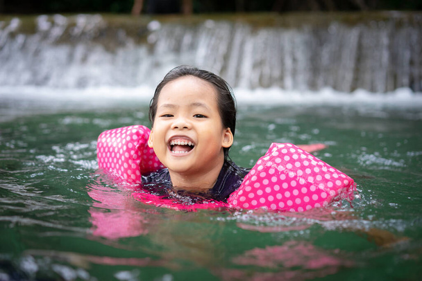 маленькая азиатская девочка с надувными рукавами, купающаяся в природной воде во время отдыха
 - Фото, изображение