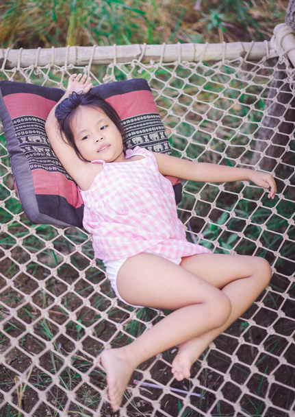 小さなアジア系の女の子がネットベンチに横になって - 写真・画像