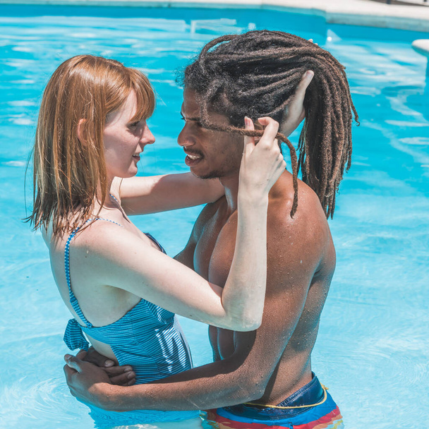 interraciale paar in het zwembad knuffelen en kijken naar elkaar - Foto, afbeelding