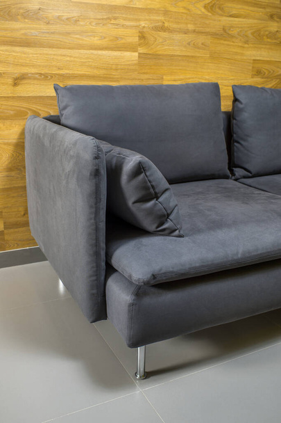 Sofá cinza com almofadas em torno de uma parede de madeira em um chão cinza - Foto, Imagem
