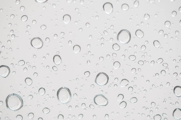 Σταγόνες βροχής στην επιφάνεια των τζαμιών Φυσικό μοτίβο σταγόνων βροχής. Φυσικό μοτίβο σταγόνων βροχής σε λευκό φόντο για το σχεδιασμό σας. - Φωτογραφία, εικόνα
