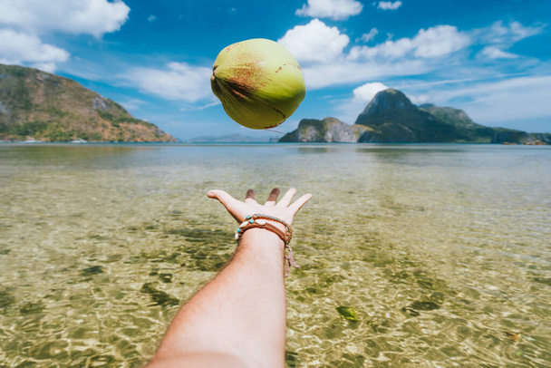 POV juggle with coconut in male hands against exotic ocean lagoon and island in background - Photo, Image