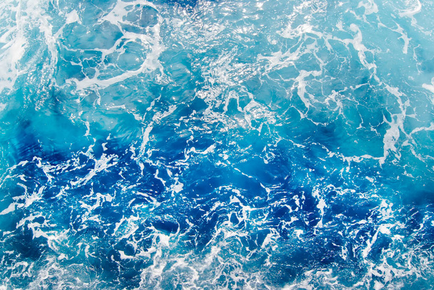 Γαλάζια αφρώδης επιφάνεια θαλασσινού νερού, πυροβολημένη στην ανοιχτή θάλασσα απευθείας από πάνω - Φωτογραφία, εικόνα