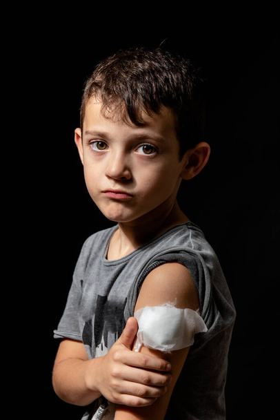 Cute little boy with sticking plaster on arm on black background - Фото, изображение