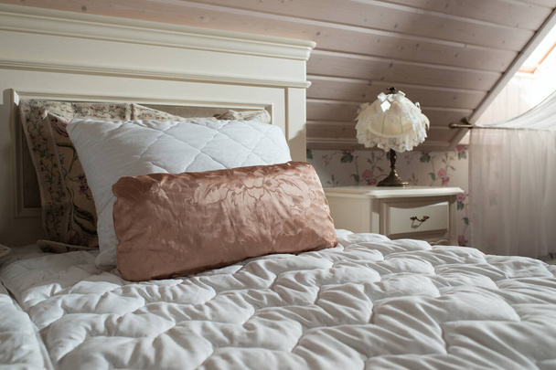窓とベッドサイドテーブルの木製のインテリアのベッドの上の枕 - 写真・画像