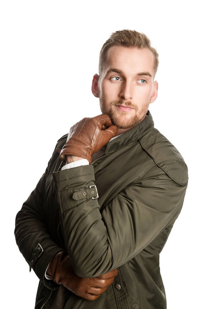 Studioshot of an attractive and confident bearded Scandinavian guywearing a waterproof green coat and brown gloves with one handon his chin isolated on white background. - Фото, зображення
