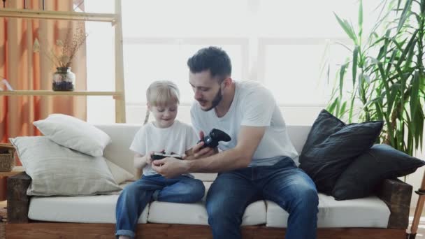 Joyful daddy and little girl playing videogame with controls in hands at home. - Materiał filmowy, wideo
