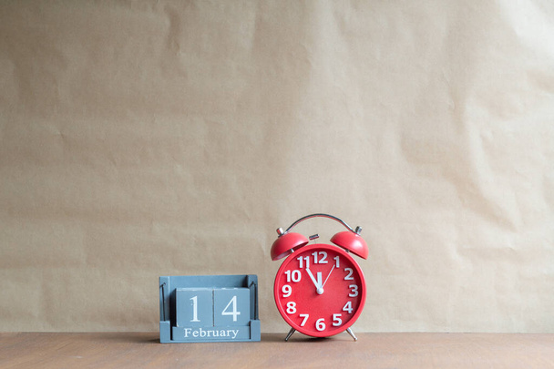 Houten kubusvormige kalender voor 14 februari met rode klok Op houten achtergrond, Retro wekker met vijf minuten tot twaalf uur. Kopieerruimte. - Foto, afbeelding
