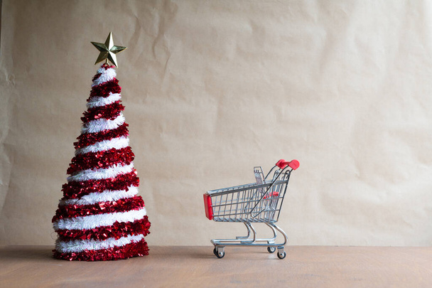 miniatuur kerstboom in een kar uit de winkel en een wekker op een winterraam, het concept van kerstverkoop - Foto, afbeelding