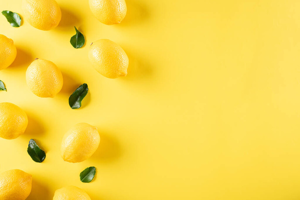 Летняя композиция выполнена из апельсинов, лимона и зеленых листьев на пастельно-желтом фоне. Фруктовый минимум. Плоская кладка, вид сверху, копировальное пространство. - Фото, изображение