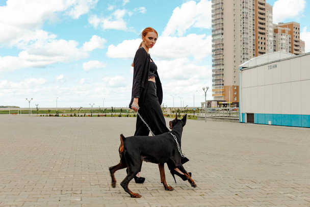 Khabarovsk, Russia - Sep 09, 2018: Fashion girl with red hair with a Doberman on the street. - Foto, imagen