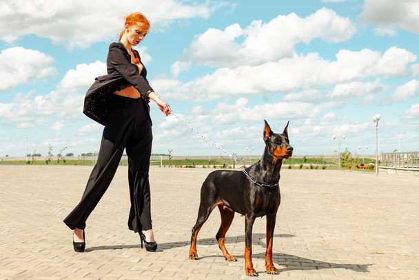 Khabarovsk, Russia - Sep 09, 2018: Fashion girl with red hair with a Doberman on the street. - Фото, изображение