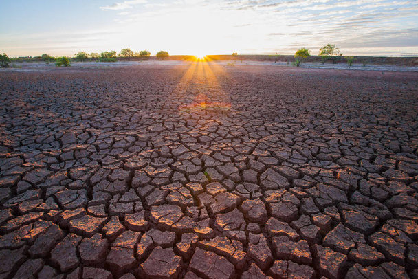 На північному сході Таїланду тріщина ґрунтів на сухому ґрунті з заходом сонця затіняє заднє місце. - Фото, зображення
