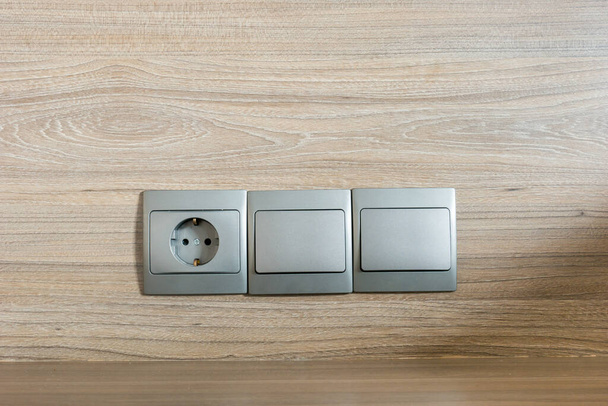 Enchufe eléctrico de color gris con fondo de madera
 - Foto, Imagen