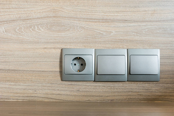 Enchufe eléctrico de color gris con fondo de madera
 - Foto, imagen