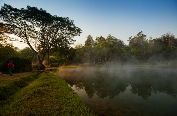 Una fuente natural de agua clara en la mañana con niebla nublada situada frente a la montaña en el norte de Tailandia. Concepto de lugar saludable
 - Foto, Imagen