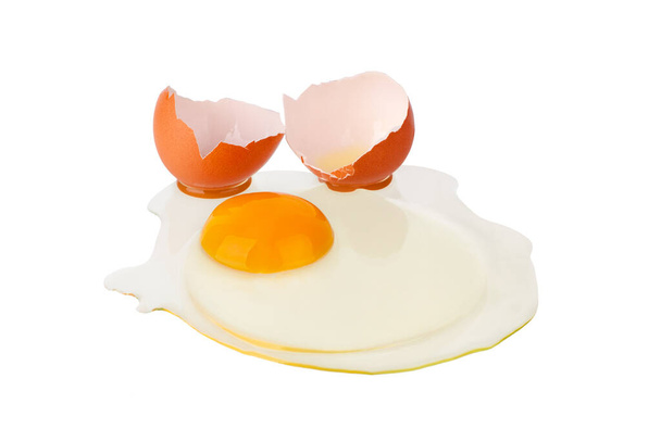 Huevo marrón roto sobre fondo blanco aislado de cerca, cáscara de huevo agrietada y huevo líquido con yema amarilla, dos mitades de cáscara de huevo macro vista superior
 - Foto, imagen