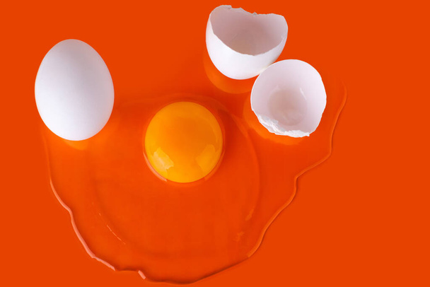 Kırık çiğ yumurta, yumurta kabuğu ve parlak turuncu arka planda tüm beyaz yumurta, üst görünümü kapat, alışılmadık tasarım, soyut kavram, Paskalya tebrik kartı, paskalya posteri - Fotoğraf, Görsel
