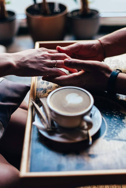 The couple in the cafe holds hands gently. A cup of coffee. - Fotoğraf, Görsel