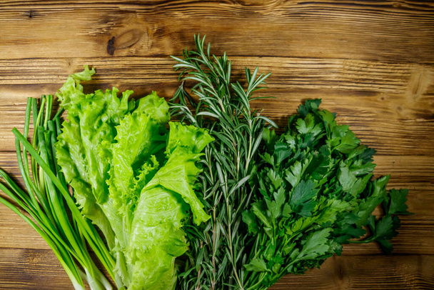 Friss petrezselyem, salátalevelek, zöldhagyma és rozmaringfűszernövények a fa asztalon. Felülnézet - Fotó, kép