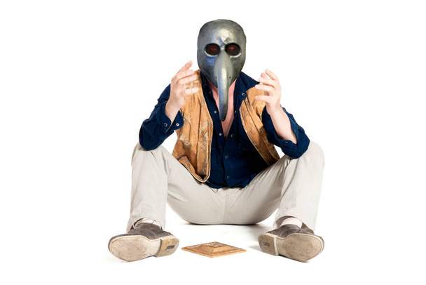Zieke oudere man met anti-pest masker en sombrero zittend op de vloer - Foto, afbeelding