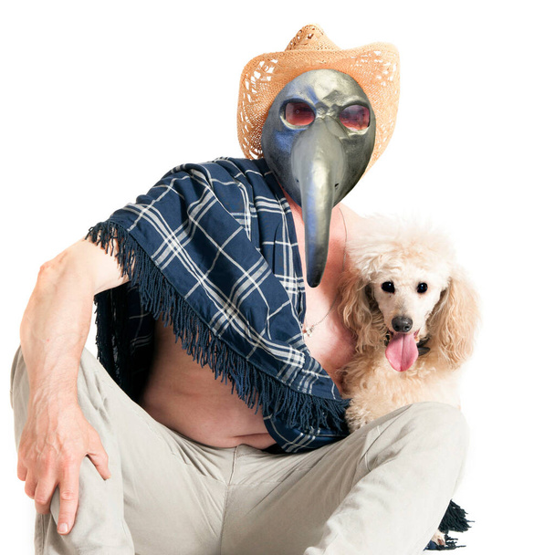 A sick elderly man in a plague mask and sombrero is sitting on the floor, hugging a poodle. - Photo, Image