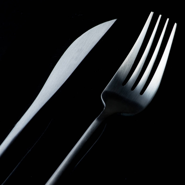 schwarze Gabel und Messer isoliert auf schwarzem Hintergrund - Foto, Bild