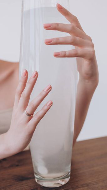 the beautiful hand of the girl with the ring on her finger encircled a vase of water - Photo, Image