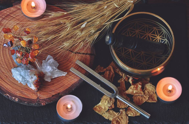 Autel sorcier wiccan préparé pour la guérison sonore magique avec fourchette de 741hz et bol chantant tibétain. Pose plate ésotérique avec plantes séchées, fleurs, cristaux, bougies allumées sur une table en bois sombre
 - Photo, image