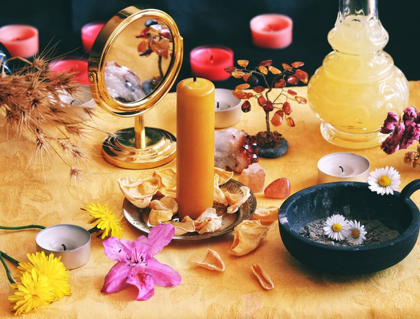 Żółta świeca na Litha święto Sabbat Święto przesilenia czarownica ołtarz pełen kwiatów, płatki róż, mniszki lekarskie, kryształy, złote lustro i inne losowe rzeczy odpowiadające Słońcu - Zdjęcie, obraz