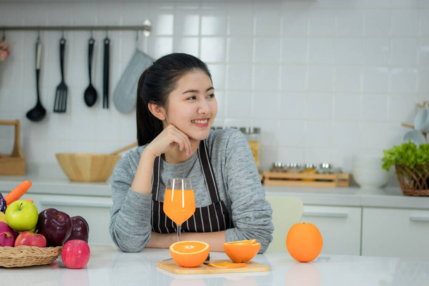 Asian young woman with glass of orange juice sitting at kitchen table,Health food concept - 写真・画像
