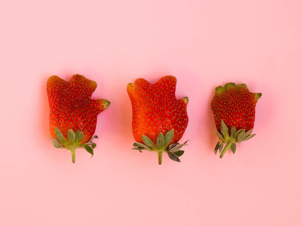 Hässliches Essen: Drei Erdbeeren auf rosa Hintergrund - Foto, Bild