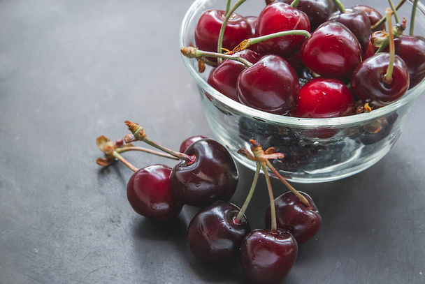 Horizontal macro picture of cherries in transparent bowl cup on black background. Summer healthy fruits concept with flat lay. Copy space for text on the left side with sweet cherry.  - Photo, Image