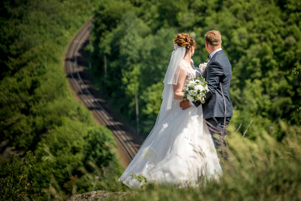 Jonge bruidspaar, bruid en bruidegom poserend op een spoorweg. Heldere zonnige dag. - Foto, afbeelding