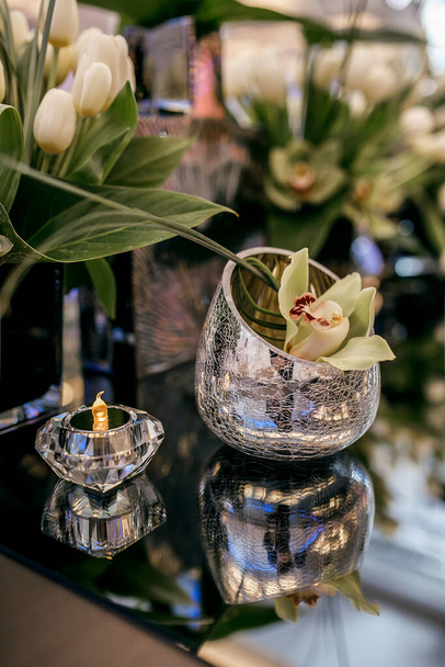 Blumen in einer Vase mit Mustern und Kerzen. Spiegelbild auf dem Tisch - Foto, Bild