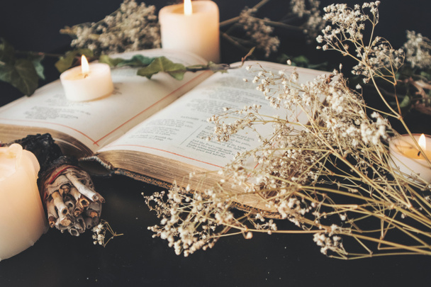 Közelkép a nyitott vintage költészeti könyv díszített szárított baba lehelet virágok. Homályos háttér fehér égő gyertyákkal, növényekkel és kis zsálya bottal. Fekete asztal felület. Romantikus lágy érzés - Fotó, kép